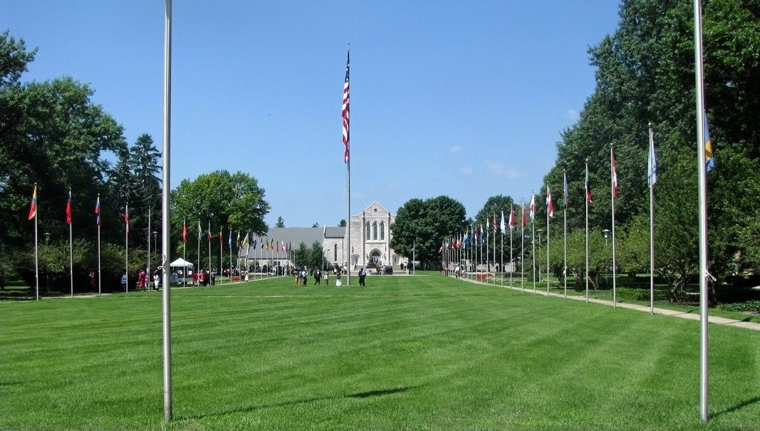 Flaggenparade auf einer gepflegten Rasenfläche vor einer historischen Kirche mit blauem Himmel, Symbol für internationale Gemeinschaft und Frieden, geeignet für christliche Veranstaltungen und religiöse Feiern.