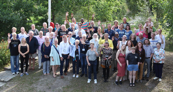 Vielfältige Gruppe von Menschen im Freien bei einer Veranstaltung, die Gemeinschaft und Zusammengehörigkeit zeigt, mit Bäumen im Hintergrund.