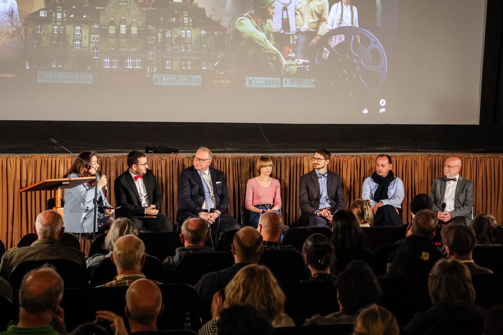 Medienpräsentation auf einer Bühne bei einer Veranstaltung, Paneldiskussion mit mehreren Sprechern, Publikum im Vordergrund, festliche und kulturelle Atmosphäre, passend für Verlag und Medienbranche.