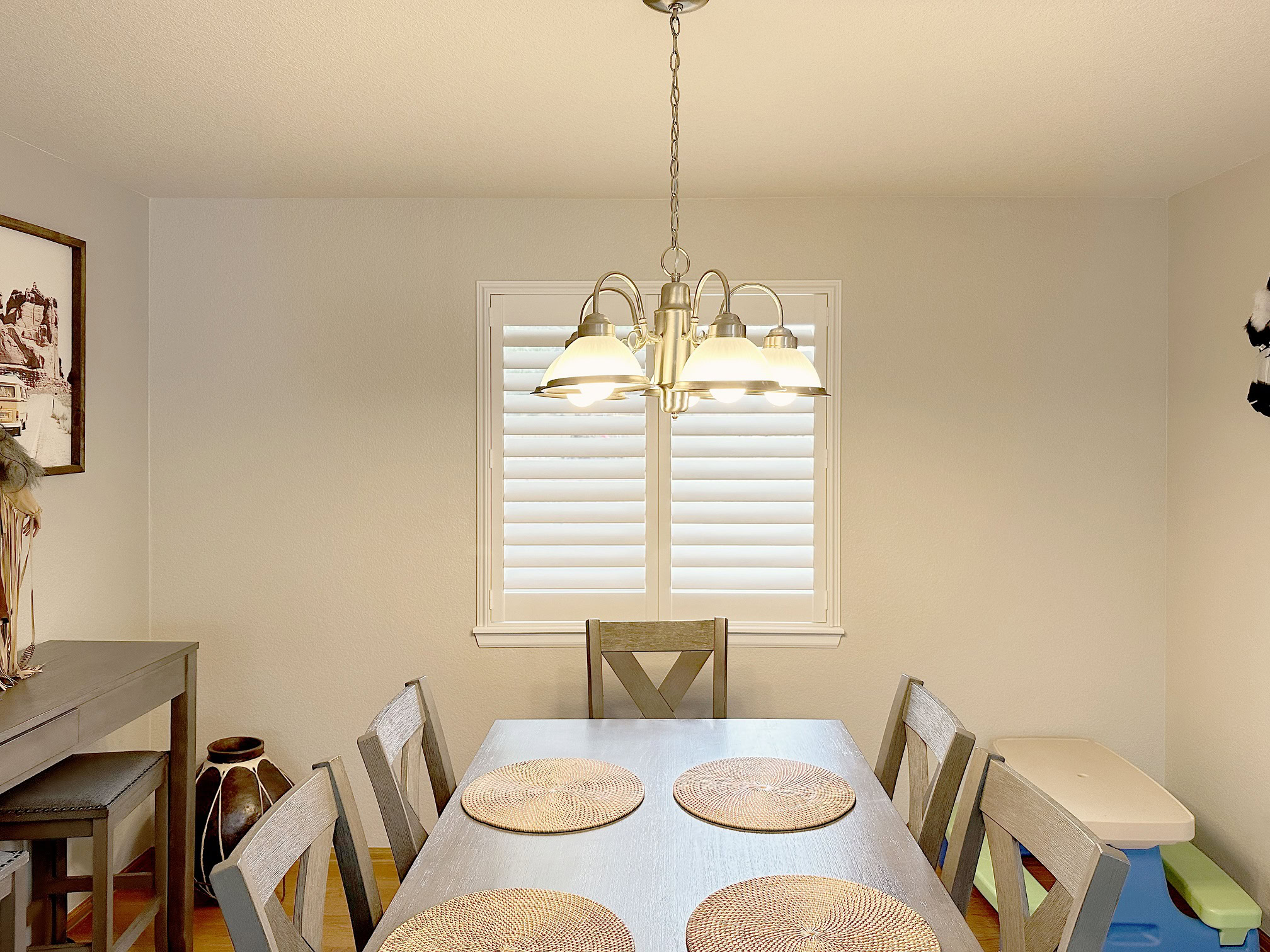 Bright dining room featuring a contemporary chandelier and large window with white shutters.