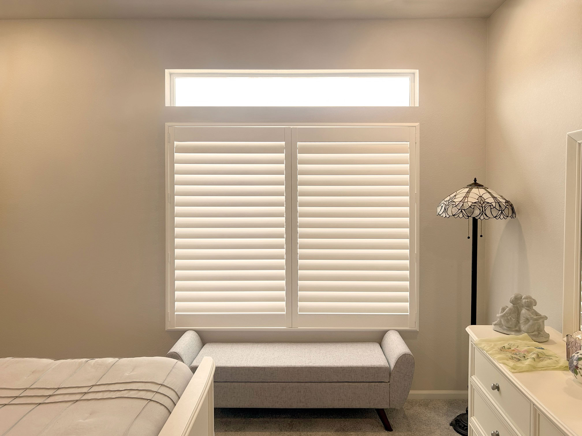 Modern window with custom shutters and a high window in a cozy bedroom setting.