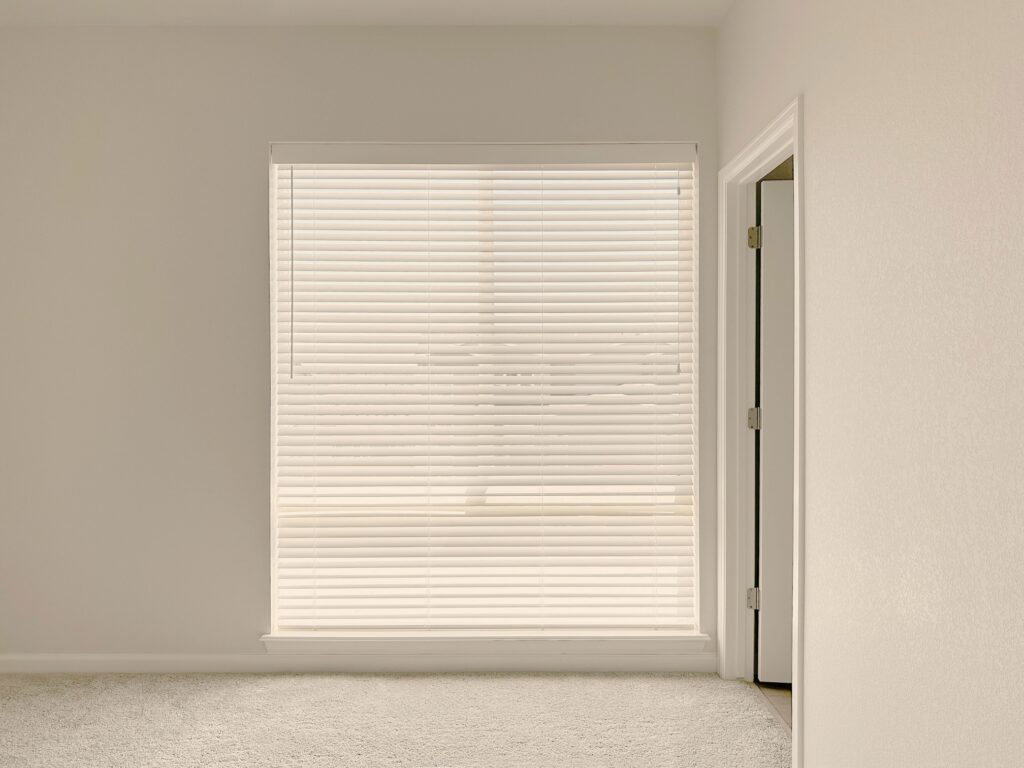 White window blinds covering a large window in a clean, modern interior.
