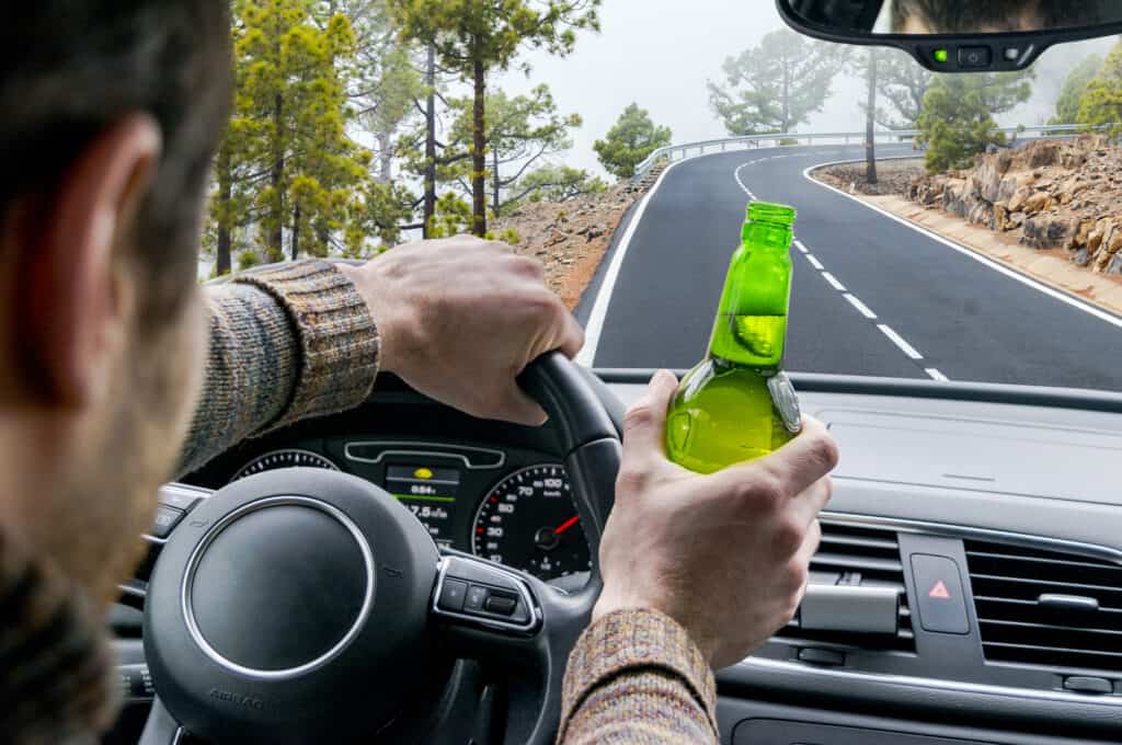 Drunk young man driving a car on the road with a bottle of beer. Don't Drink and drive. Drunk driving under the influence. Driving while intoxicated. Dangerous drunk driving concept.