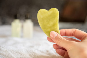 Hand holding jade Gua Sha massage stone.