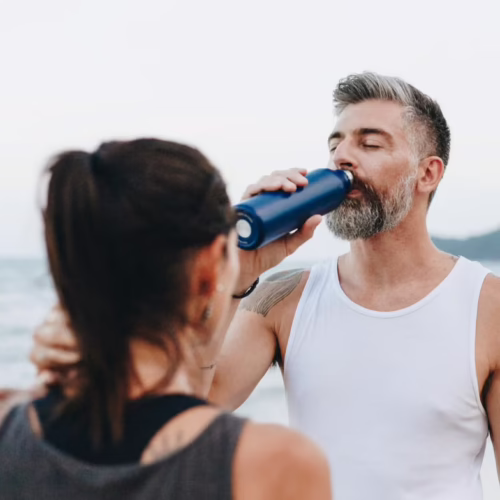 Man drinking water outdoors during summer activity, representing hydration, electrolytes, heat, and healthy summer habits