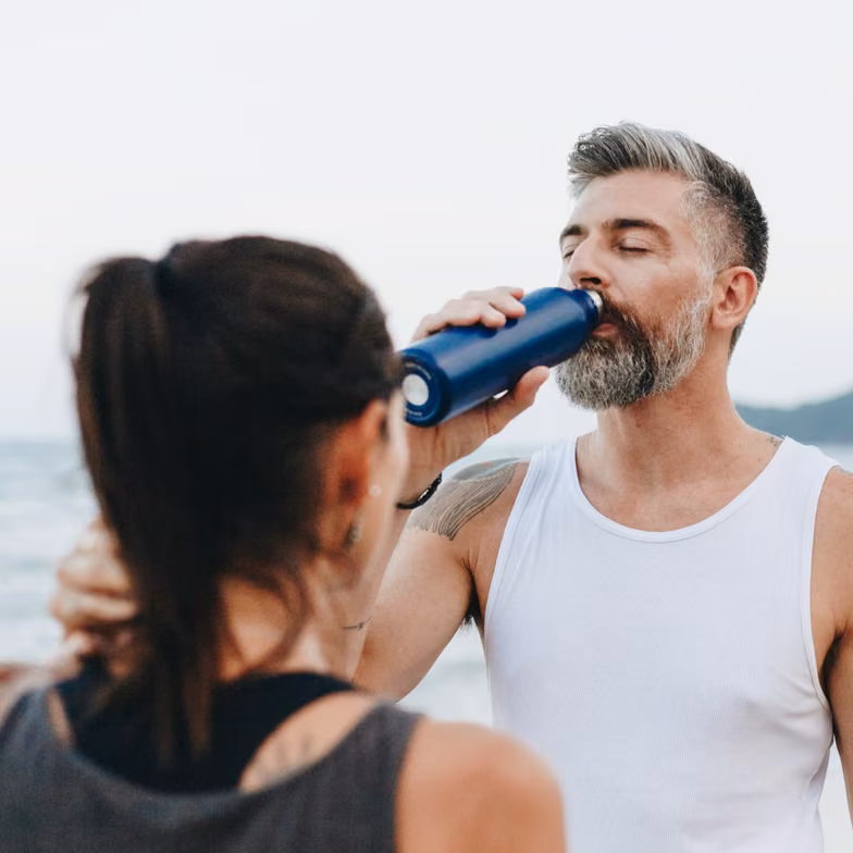 Man drinking water outdoors during summer activity, representing hydration, electrolytes, heat, and healthy summer habits