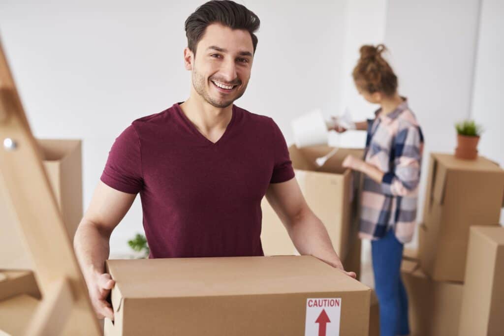 Happy mover holding a cardboard box in a modern home setting.