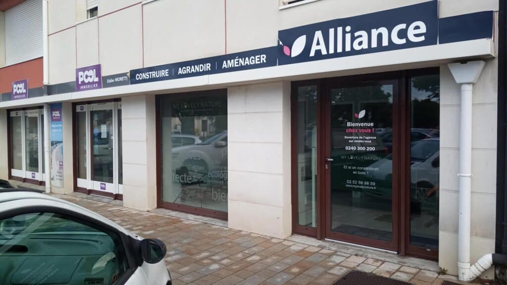 agence-pornichet Façade d’une agence Alliance située à Pornichet, avec une enseigne affichant les services de construction, agrandissement et aménagement, accompagnée de vitrines modernes et d’un accueil chaleureux pour les visiteurs.