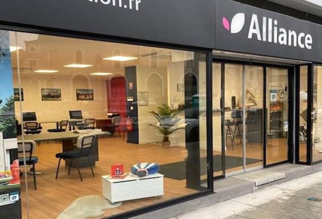 Façade de l'agence Alliance située à Angers, avec de grandes vitrines laissant apparaître un intérieur moderne et chaleureux, aménagé avec des espaces de travail et de réunion lumineux.