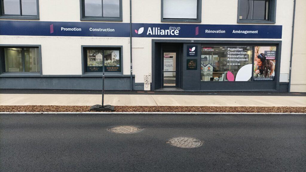 agence-laroche Façade d’une agence Alliance Group affichant ses services de promotion, construction, rénovation et aménagement, avec des vitrines informatives et une signalétique professionnelle, située dans un environnement urbain