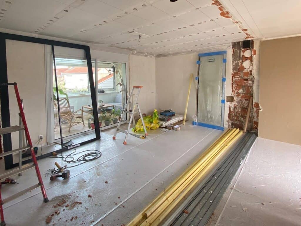 Pièce en pleine rénovation avec préparation des murs, pose des structures de plafond et aménagement d’une baie vitrée donnant sur une véranda lumineuse. Un chantier prometteur pour un intérieur moderne et fonctionnel.