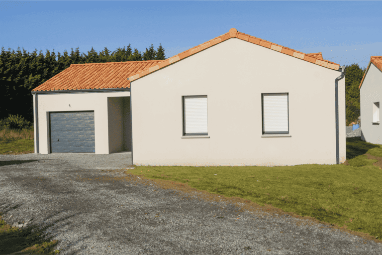 Maison de plain-pied en crépi beige avec toit en tuiles rouges, garage intégré et allée en gravier sur terrain arboré.