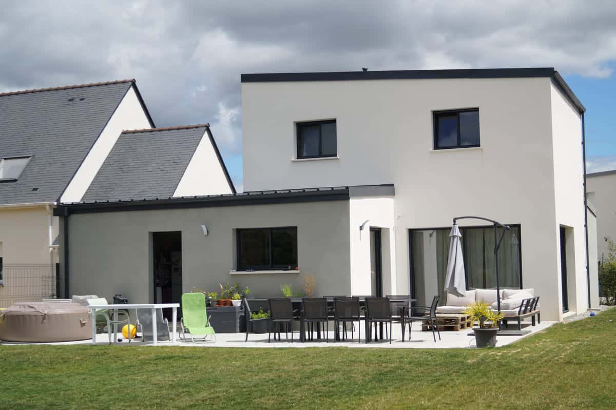 Maison contemporaine à étage avec toit plat, crépi blanc et gris, grande terrasse aménagée et jardin spacieux.