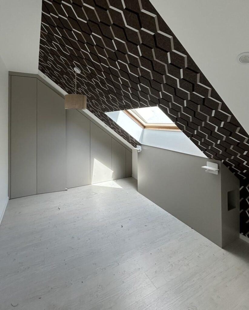 Aménagement sous combles avec des rangements intégrés et un papier peint géométrique au plafond, éclairé par une fenêtre de toit pour une ambiance lumineuse et contemporaine.