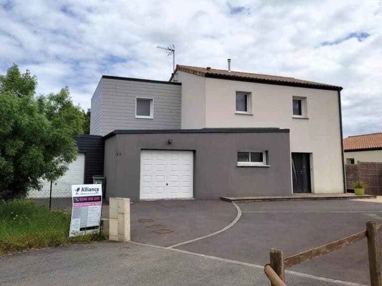 Maison après travaux, avec une façade blanche simple et un toit en tuiles rouges. Le jardin offre une pelouse bien entretenue et une terrasse en bois, créant un espace extérieur convivial en attente d'une modernisation et d'une extension pour optimiser le style et la fonctionnalité.