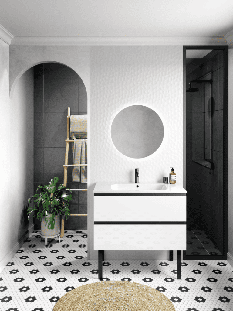Une salle de bain contemporaine et raffinée, mettant en valeur un meuble blanc brillant aux lignes épurées, avec un miroir circulaire rétroéclairé pour une ambiance douce et moderne. Le carrelage hexagonal noir et blanc au sol apporte une touche graphique élégante, tandis que les murs texturés et l’arche ajoutent de la profondeur à l’espace. Une douche à l'italienne avec une paroi en verre noir complète ce design harmonieux. L’ajout d’éléments naturels, comme la plante verte et l’échelle en bois, apporte une note chaleureuse et apaisante.
