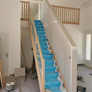 Installation d'un escalier avec protection en film bleu pendant la phase de finition.