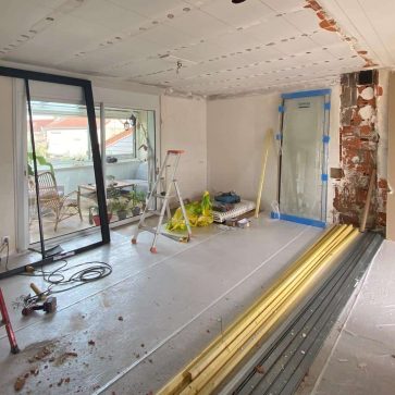 Pièce en pleine rénovation avec préparation des murs, pose des structures de plafond et aménagement d’une baie vitrée donnant sur une véranda lumineuse. Un chantier prometteur pour un intérieur moderne et fonctionnel.