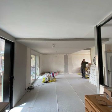 Vue d’un intérieur en cours de rénovation avec des cloisons en placo, de grandes baies vitrées apportant de la lumière naturelle et un espace ouvert en transformation. Un chantier prometteur pour un aménagement moderne et fonctionnel.