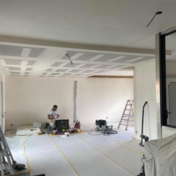 Travaux d'aménagement intérieur avec plafonds en placo en phase de finition et murs prêts à être peints. Un espace ouvert lumineux en pleine rénovation, promettant un design moderne et épuré.