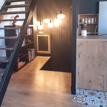 Aménagement intérieur moderne avec un escalier en métal et bois, un coin lecture éclairé par des suspensions design, et un sol combinant parquet clair et carreaux de ciment. Une harmonie parfaite entre style industriel et chaleureux.