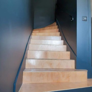 Escalier moderne en bois clair avec murs peints en noir mat, créant un contraste élégant et minimaliste. Un design épuré et contemporain pour une transition harmonieuse entre les étages.