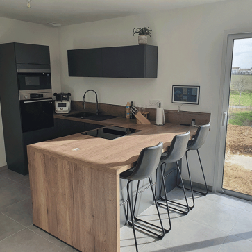 Cuisine moderne en U avec plan de travail en bois et bar avec trois chaises.