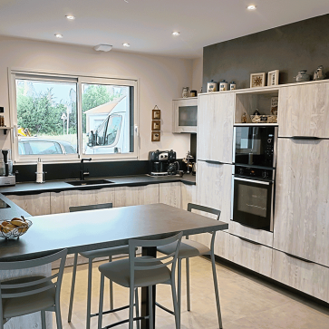 Cuisine moderne avec implantation en U, meubles en bois clair, espace lumineux.