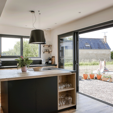 Cuisine moderne avec ilôt central et grandes fenêtres offrant une vue extérieure.