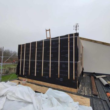 Travaux en cours sur une maison, montrant la construction d'une ossature en bois pour une extension ou une surélévation. Mise en place de l'isolant ECOTECH 200 et préparation pour l'installation du bardage, soulignant l'usage de matériaux modernes et performants.