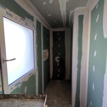 Avancée d'une rénovation intérieure avec des murs en plaques de plâtre vertes (hydrofuges) en cours de jointoiement. La pièce est équipée d'une fenêtre à vitrage dépoli et d'une niche murale, annonçant une future salle d'eau fonctionnelle et moderne.