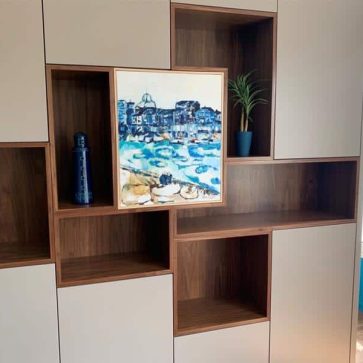 Bibliothèque moderne avec niches en bois noyer et façades blanches, intégrant une œuvre d'art et des éléments décoratifs. Une solution élégante et fonctionnelle pour un espace à la fois pratique et esthétique.