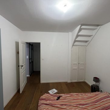 Chambre lumineuse avec parquet en bois massif et rangement intégré sous un escalier, parfait pour optimiser l'espace dans un projet de rénovation intérieure.