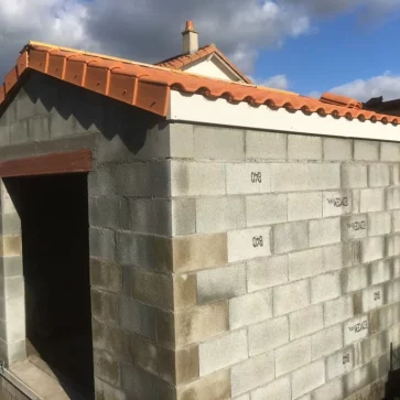 Cette construction en parpaings, destinée à être un espace annexe, a été soigneusement réalisée avec une toiture en tuiles pour une parfaite harmonie avec le bâti existant. Les finitions de toiture, notamment les débords, apportent une touche esthétique tout en garantissant une protection optimale contre les intempéries. Un projet fonctionnel et durable.