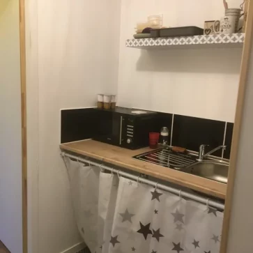 Cette kitchenette a été aménagée pour allier praticité et charme. Le plan de travail en bois apporte une touche naturelle, complété par des rideaux à motifs étoilés qui dissimulent les rangements inférieurs. Les carreaux de ciment au sol ajoutent du caractère et délimitent visuellement l’espace. Un aménagement optimisé pour les petits espaces.