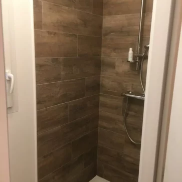Cette douche a été entièrement rénovée avec un carrelage effet bois pour une ambiance chaleureuse et naturelle. La robinetterie moderne et le receveur plat apportent un confort et une esthétique contemporaine à cet espace.