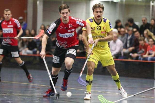 Hockeyspieler im intensiven Spiel auf Indoor-Feld, Fans im Hintergrund, sportliche Action, UHC Alligator Malans, Teamwettbewerb, dynamisches Spiel.