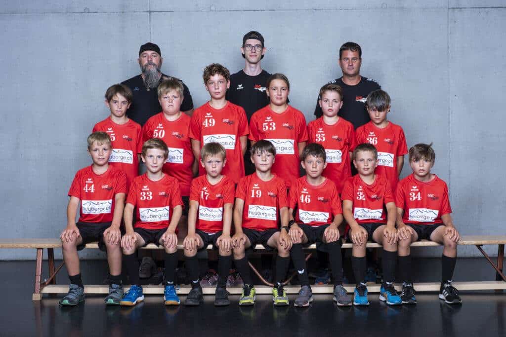UHC Alligator Malans Jugendhandballteam, Kinder mit roter Sportswear, Mannschaftsfoto indoor.