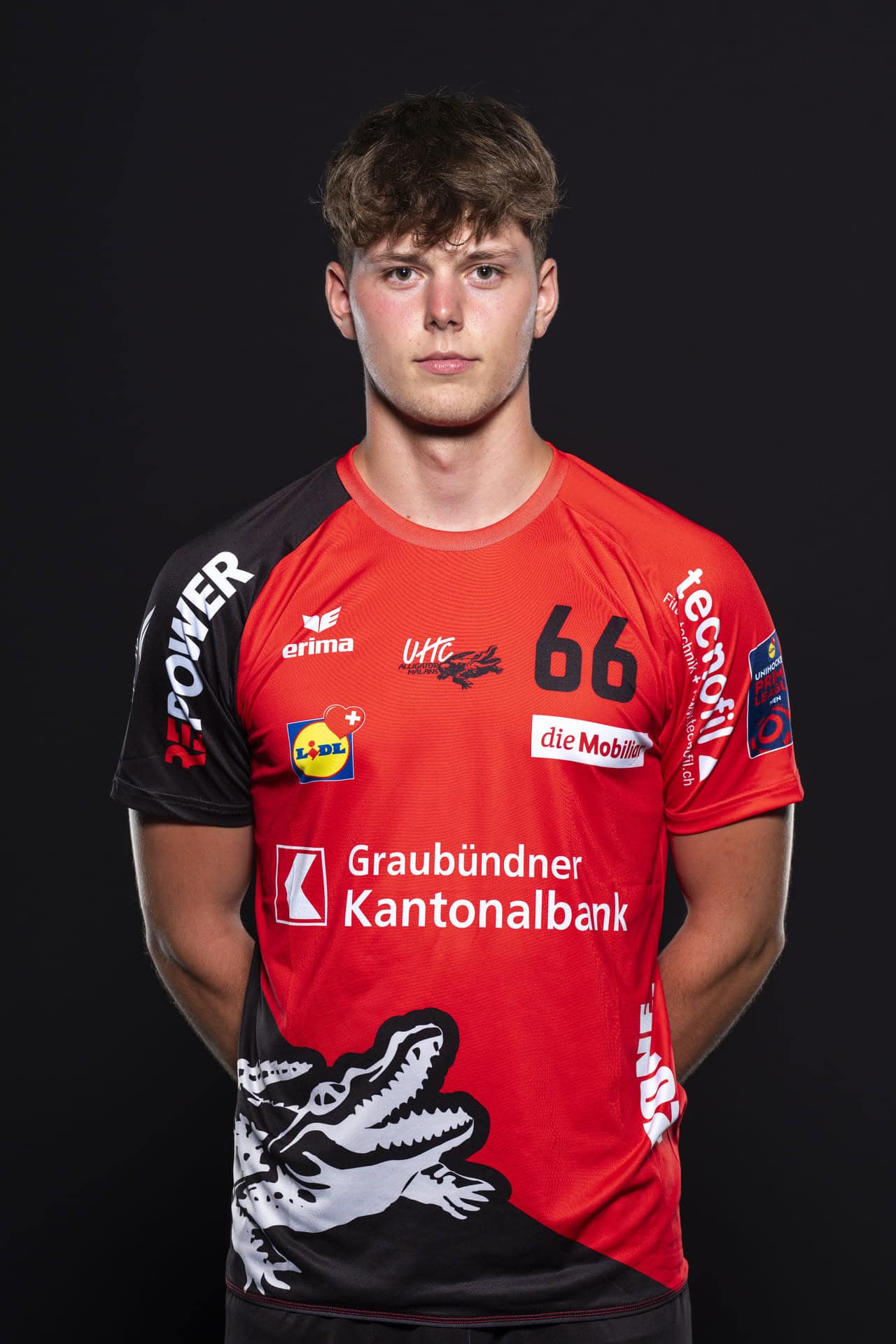 Junge Handballspieler in rotem UHC Alligator Malans Trikot, professionell, auf schwarzem Hintergrund.