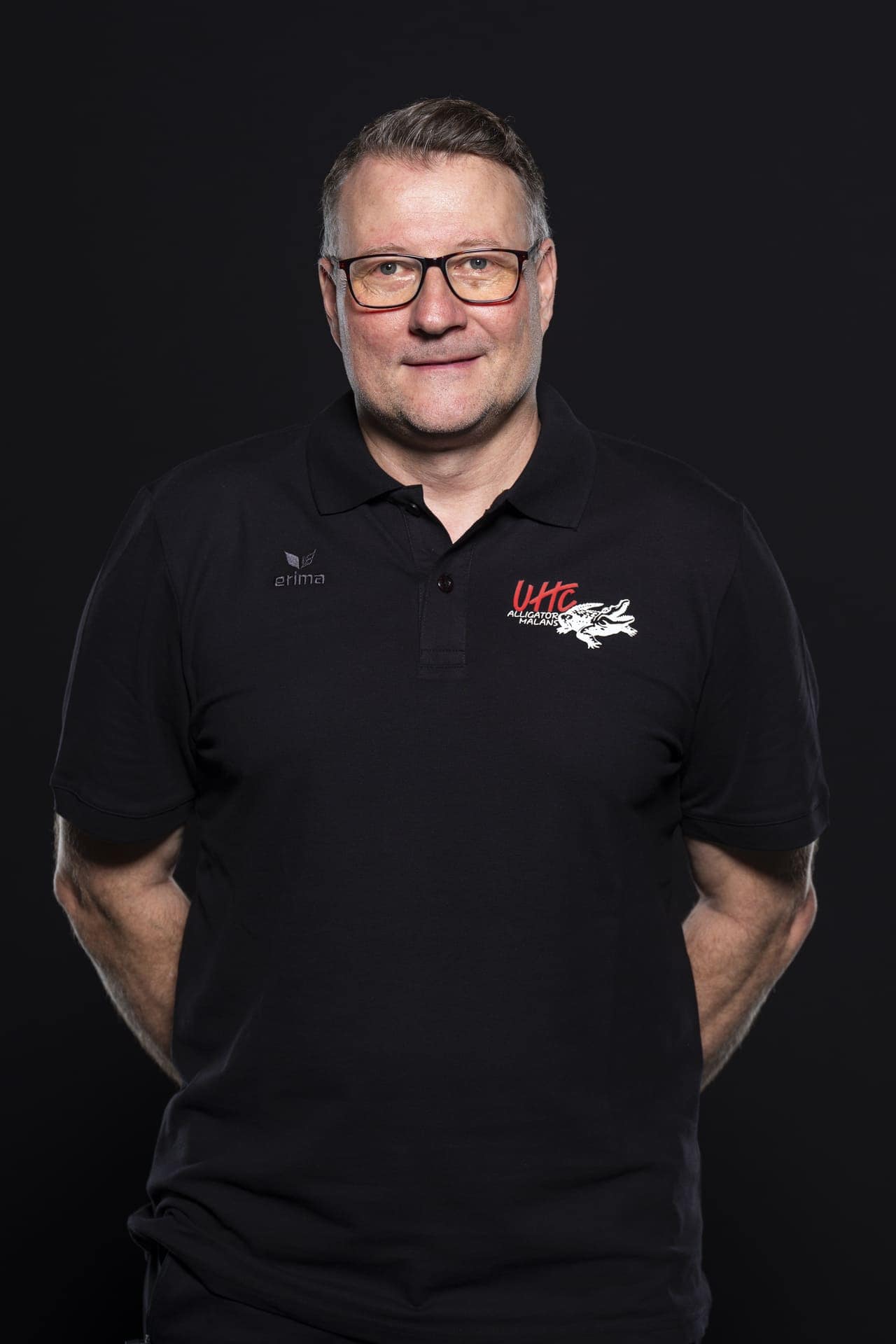 Mann in schwarzen UHC Alligator Malans Polo-Shirt vor schwarzem Hintergrund.