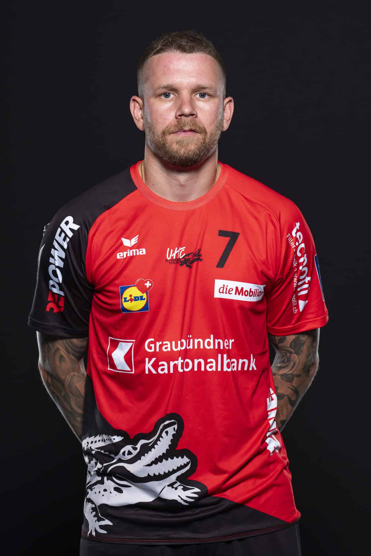 UHC Alligator Malans Volleyballspieler in rotem Trikot mit Nummer 7, professionell posaunend im Portrait.