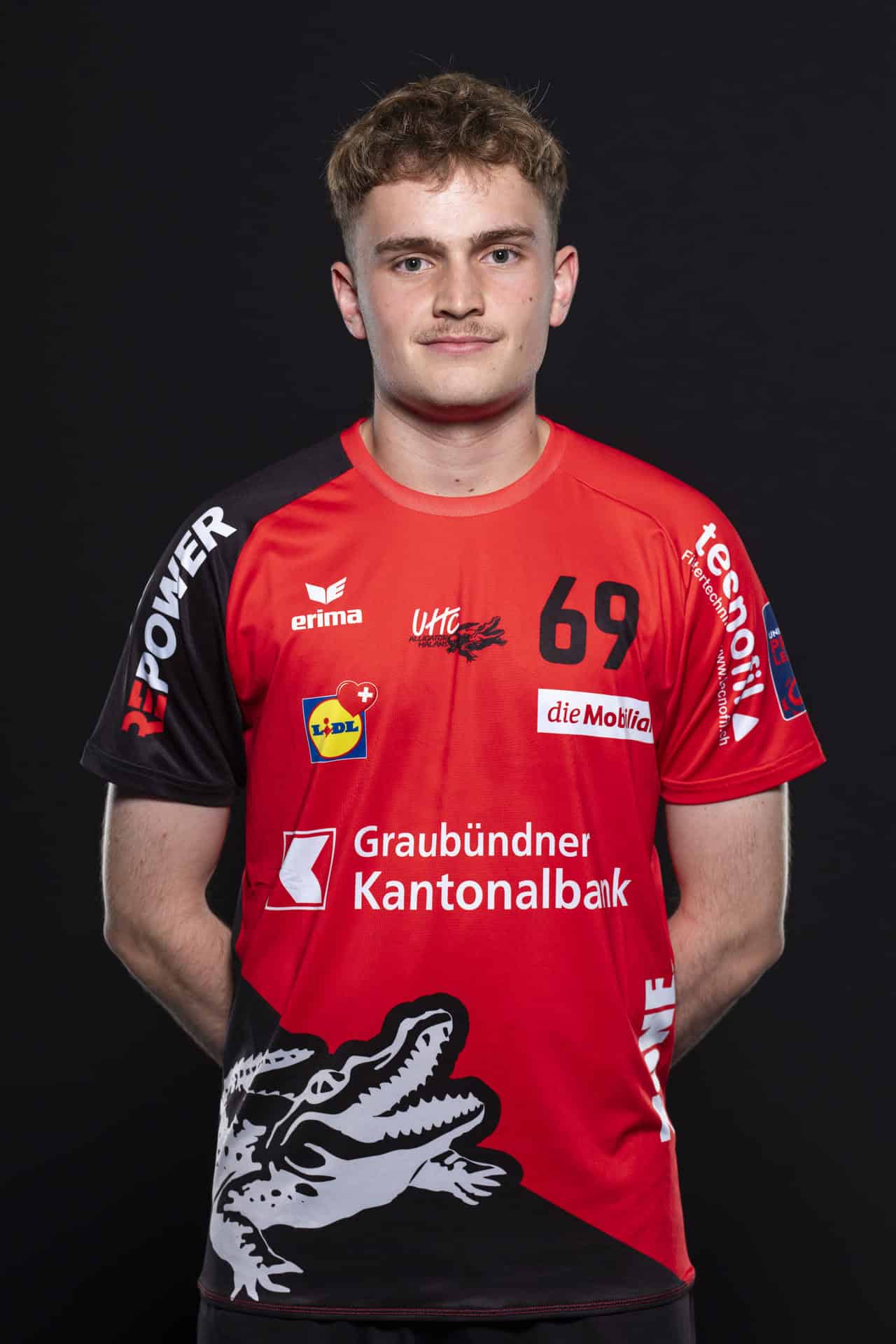 UHC Alligator Malans Handballspieler in Rot mit Trikotsponsor und Logo vor schwarzem Hintergrund.