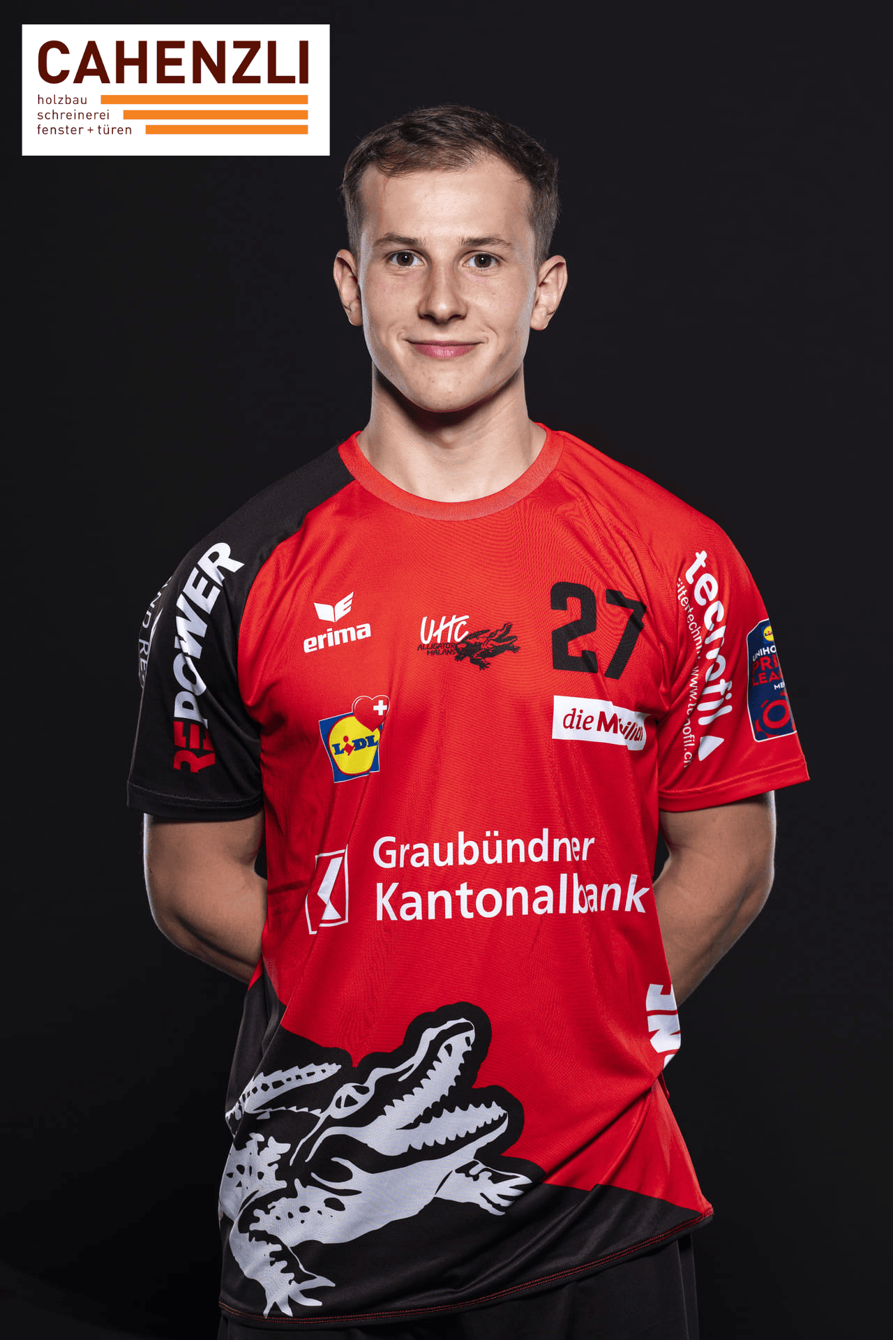 UHC Alligator Malans Spieler in rotem Mannschaftstrikot mit Alligator Logo, Nummer 27, gegen schwarzem Hintergrund, Sponsorenlogos sichtbar, sportliches Portrait, Volleyballverein in Graubünden.