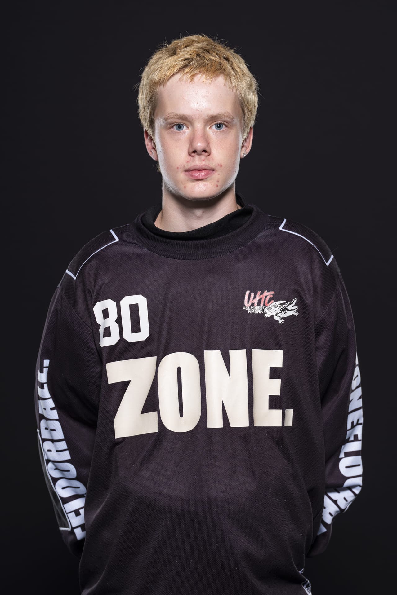 Junges Eishockeyspieler mit blondem Haar im schwarzen UHC Alligator Malans Trikot, Portrait vor dunklem Hintergrund.