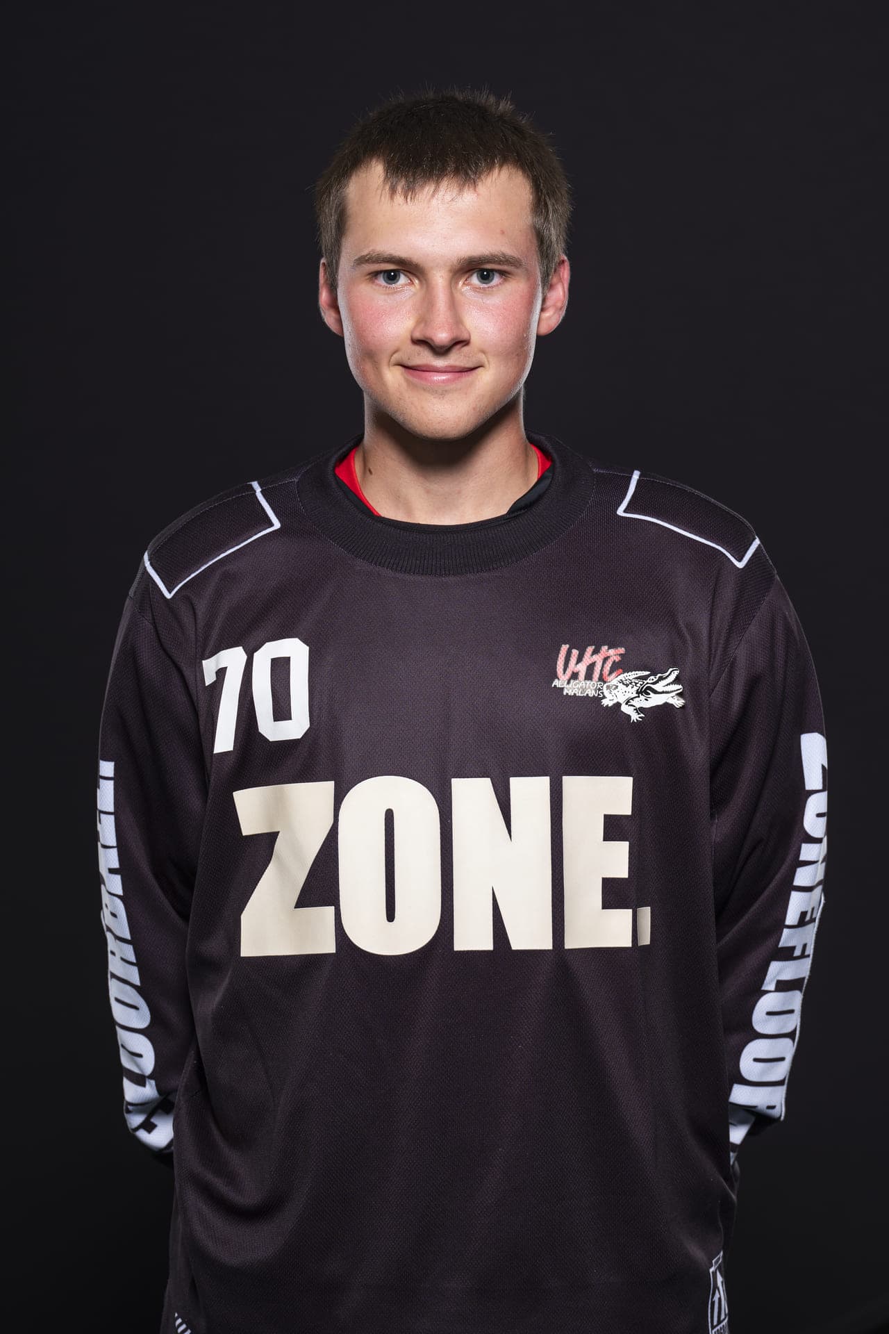 Junge männliche Eishockeyspieler in UHC Alligator Malans Trikot, lächelt freundlich, professioneller Kopfshot vor schwarzem Hintergrund.