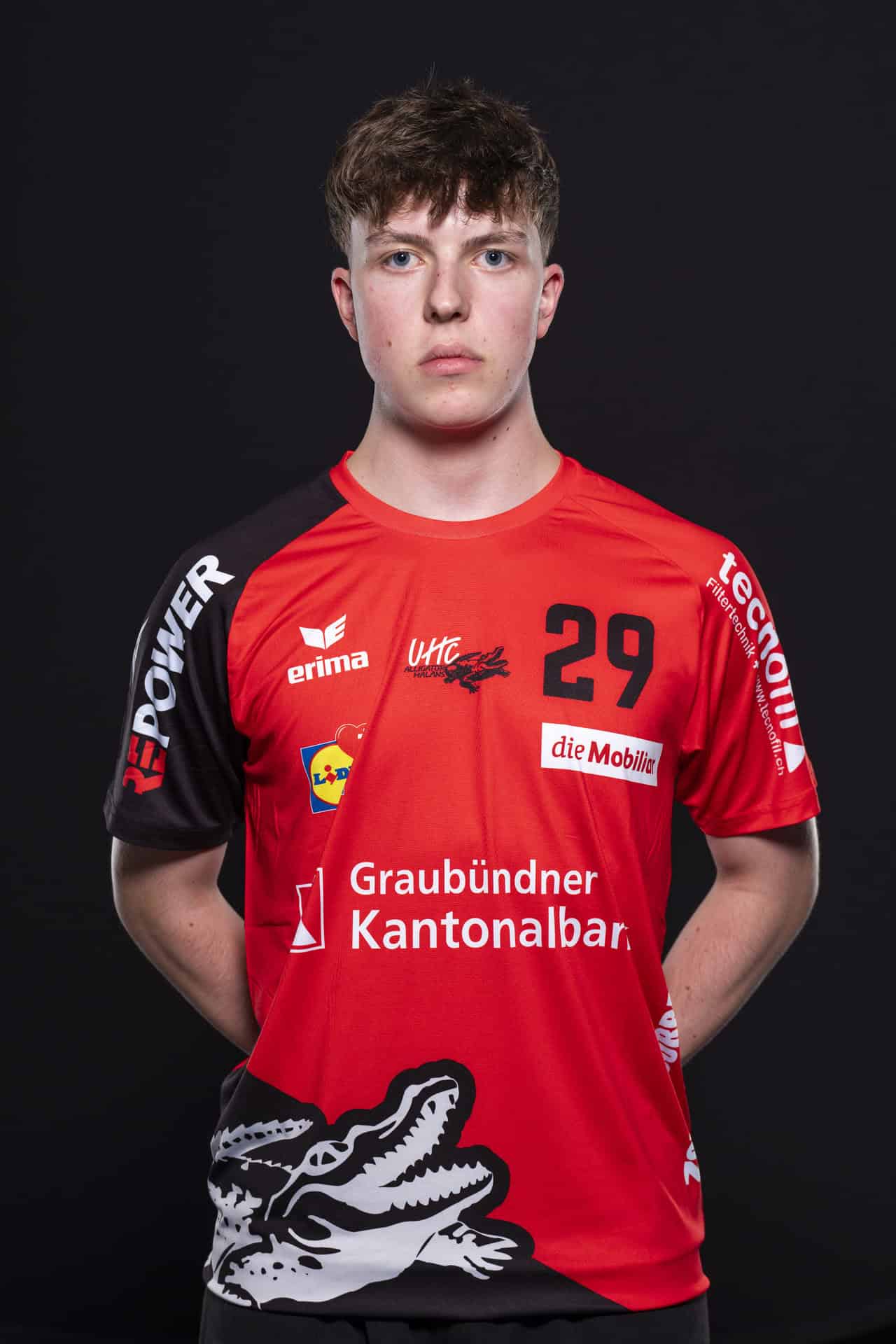 UHC Alligator Malans Volleyballspieler in rotem Trikot mit schwarzen Logo-Details vor dunklem Hintergrund.