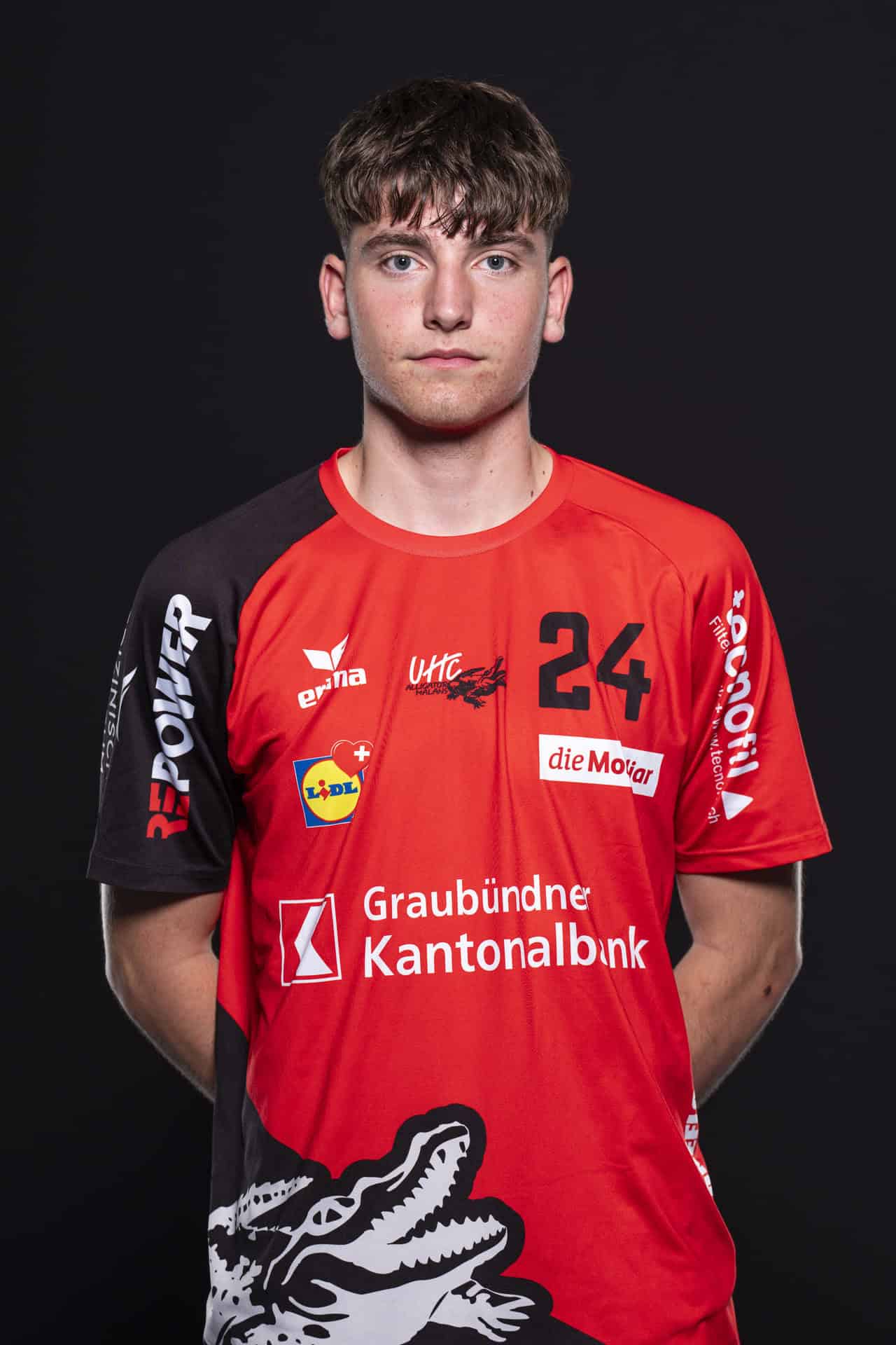 Hervorgehobenes Bild eines jungen männlichen Volleballspielers in rotem UHC Alligator Malans Trikot, bereit für den Einsatz, gegen einen schwarzen Hintergrund.