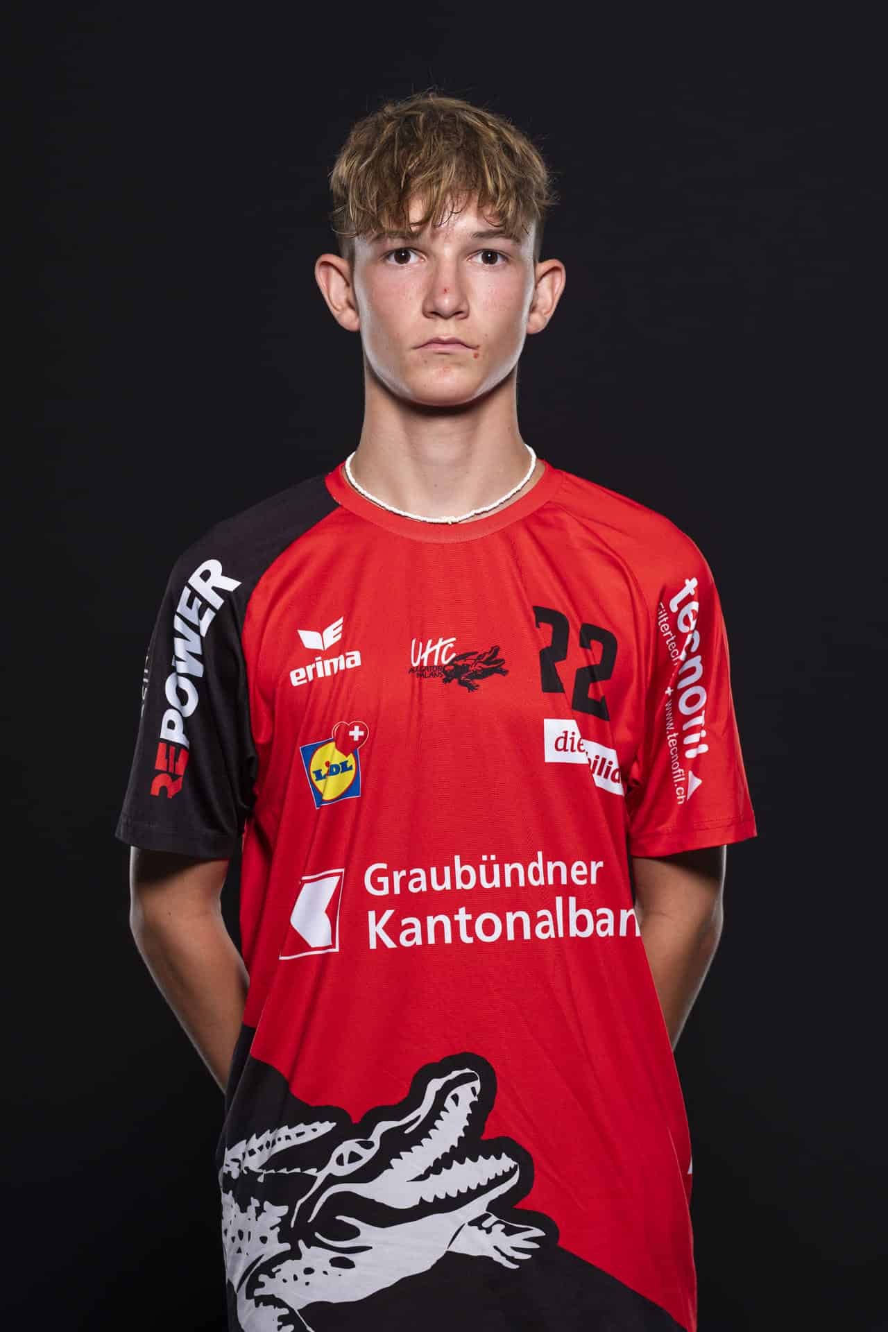 Junger Handballspieler in UHC Alligator Malans Trikot, Frontansicht, sportliche Pose, individuelle Portraitaufnahme, Indoor-Photo, schweizerischer Handballsport, Teamspieler, Vereinslogo sichtbar, jugendliche Athletik, Handballteam.