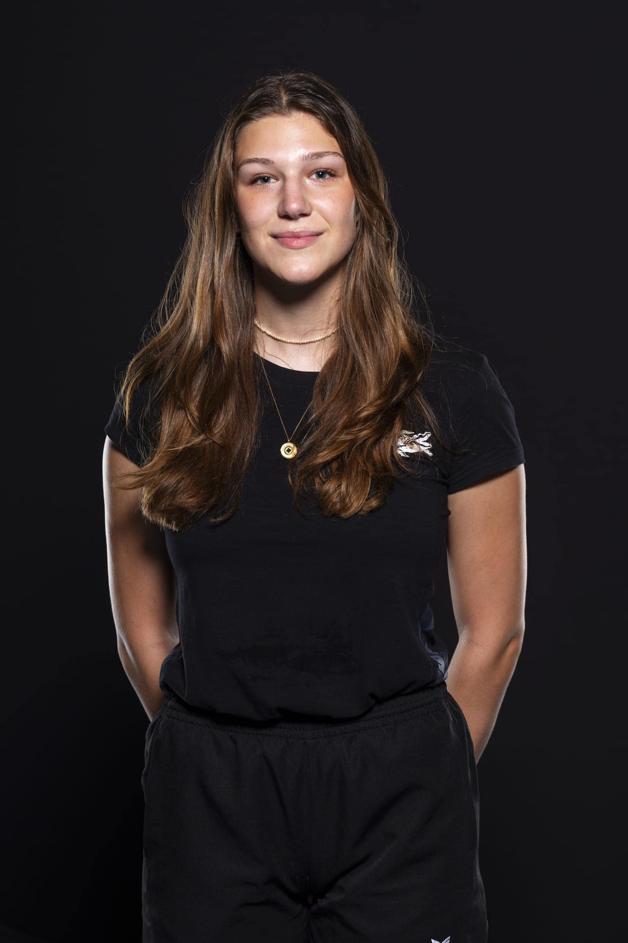 Starkes Bild einer jungen Frau mit langen braunen Haaren in Blackoutfit, die für das UHC Alligator Malans Team wirbt. Perfekte Team-Fotografie für die Floorball- oder Eishockey-Mannschaft.