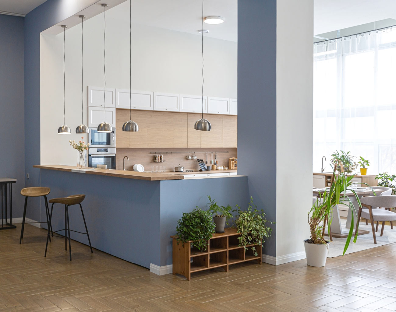 Moderne cuisine lumineuse avec plantes, comptoirs en bois clair, tabourets et suspensions.